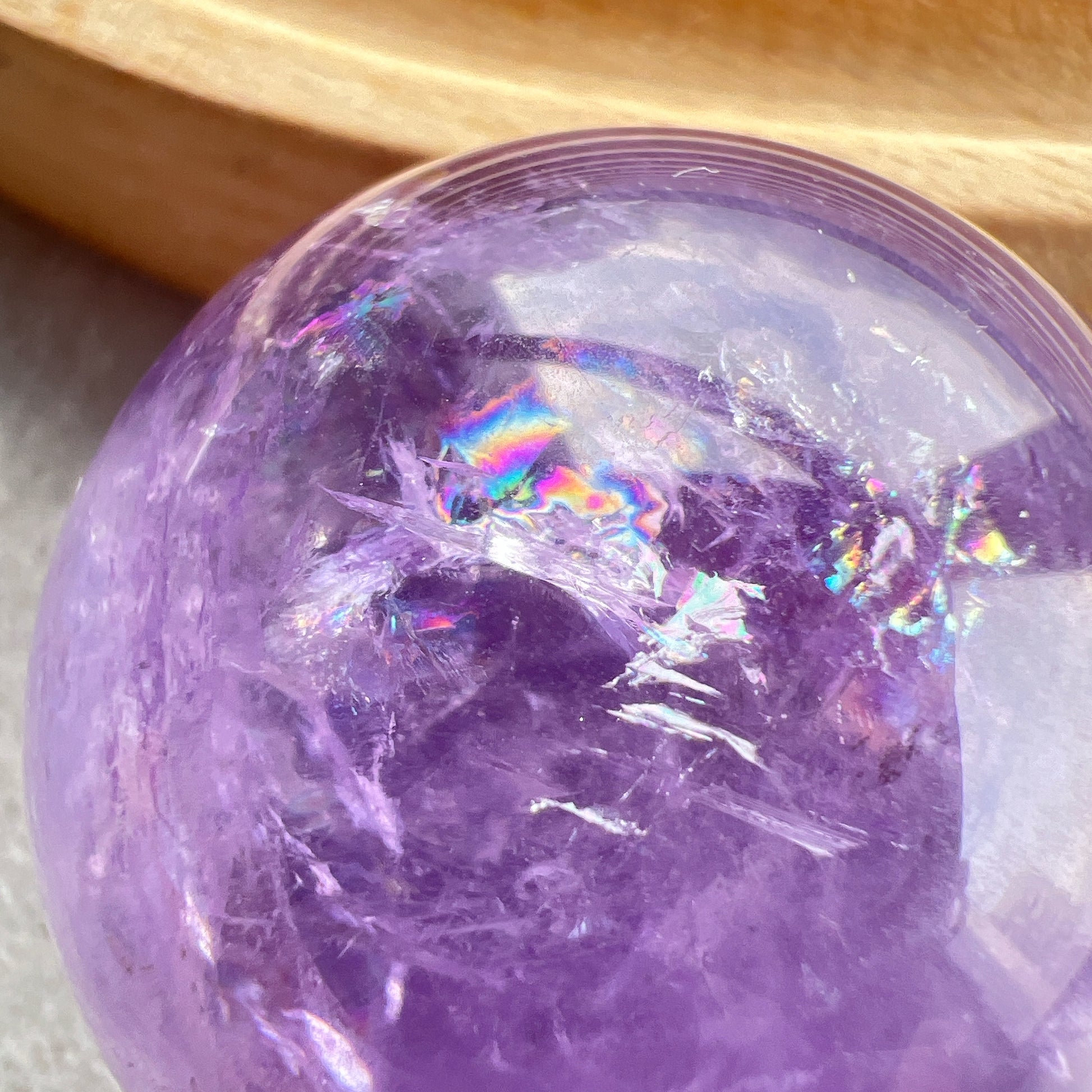 紫水晶
【 圓潤之境，光之詩意 】｜ 彩虹光紫水晶球

如果說隨形是自然的率性，那麼水晶球便是大地最圓滿的溫柔。

這顆紫水晶球在純淨的紫色晶體中，包裹著歲月沈澱的天然冰裂紋與雲霧。 透過自然光線的折射，球體內部在不同角度下會閃耀出如夢似幻的彩虹光芒，彷彿將雨後的晴空濃縮於指尖。
