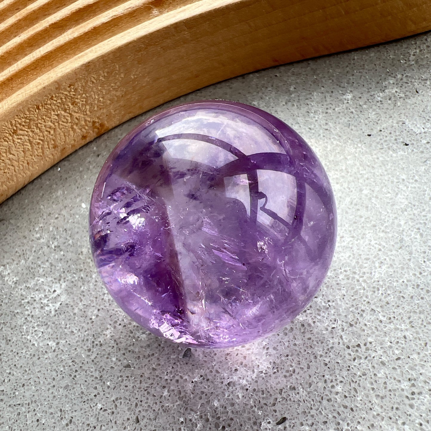 紫水晶
【 圓潤之境，光之詩意 】｜ 彩虹光紫水晶球

如果說隨形是自然的率性，那麼水晶球便是大地最圓滿的溫柔。

這顆紫水晶球在純淨的紫色晶體中，包裹著歲月沈澱的天然冰裂紋與雲霧。 透過自然光線的折射，球體內部在不同角度下會閃耀出如夢似幻的彩虹光芒，彷彿將雨後的晴空濃縮於指尖。