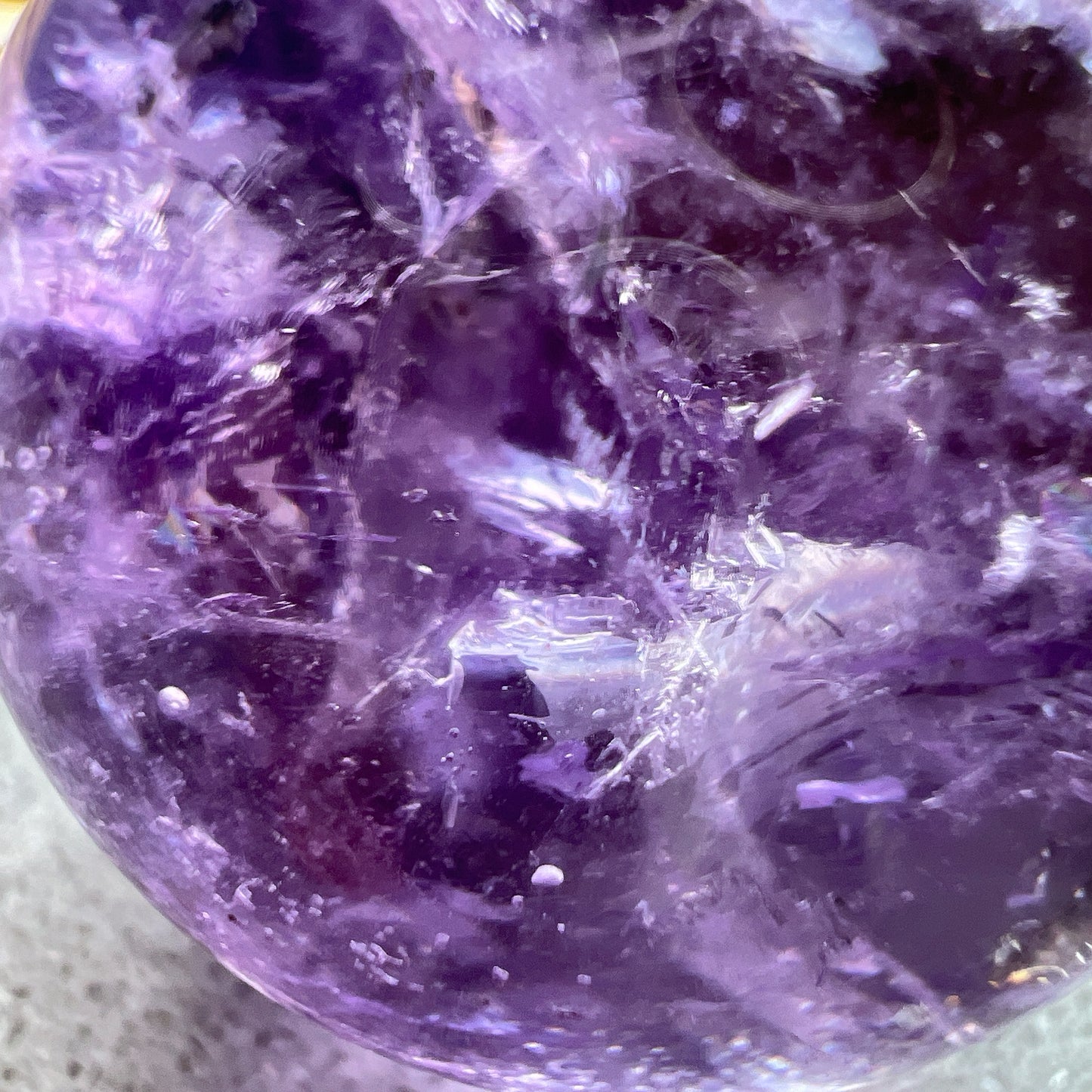 紫水晶
【 圓潤之境，光之詩意 】｜ 彩虹光紫水晶球

如果說隨形是自然的率性，那麼水晶球便是大地最圓滿的溫柔。

這顆紫水晶球在純淨的紫色晶體中，包裹著歲月沈澱的天然冰裂紋與雲霧。 透過自然光線的折射，球體內部在不同角度下會閃耀出如夢似幻的彩虹光芒，彷彿將雨後的晴空濃縮於指尖。